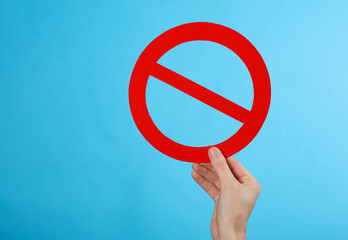 Hand holding red prohibition sign on a blue background