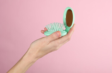 Woman's hand holds mirror comb on a pink background. Beauty concept