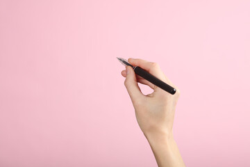 Female hand writes with pen on a pink background. Template for design