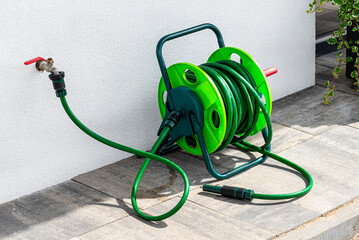 A garden hose connected to a faucet protruding from a building against a white facade..