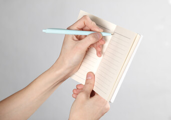 Female hand writing in notebook on gray background
