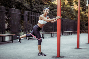 Young muscular woman trains muscles with fitness rubber bands on a sports workout ground. Healthy lifestyle. Fitness and bodybuilding. Resistance training