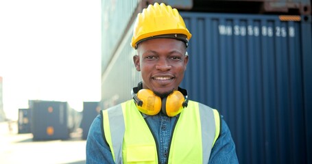 Handsome professional African engineers worker wearing a safety vest and hard hat charmingly smiling on camera. In the logistics warehouse background