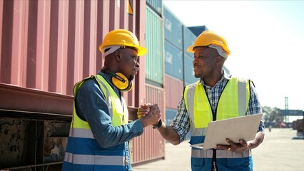 Two professional African engineers wearing safety uniforms and helmets shaking hands to ensure work after successful dealing at warehouse