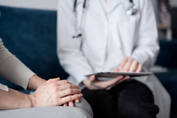 Doctor and patient sitting at sofa in clinic office. The focus is on female woman's hands, close up. Medicine concept