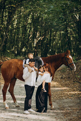 Young family with kids having fun with horse in forest