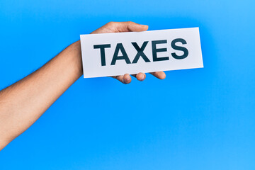 Hand of caucasian man holding paper with taxes word over isolated blue background