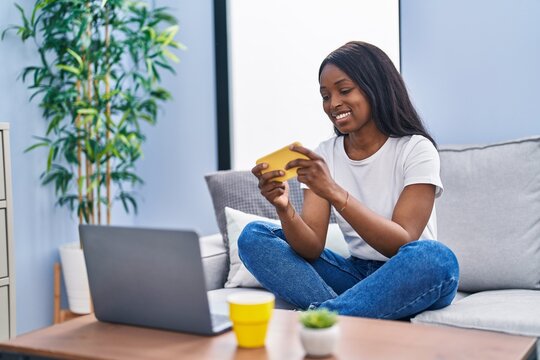 Young african american woman playing video game sitting on sofa at home