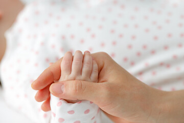 Close up mother holding tiny hand of little newborn baby boy girl, helping hands, bonding different generations. Happy motherhood concept.