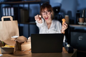 Young beautiful woman working using computer laptop and eating delivery food pointing displeased and frustrated to the camera, angry and furious with you