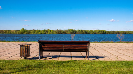 Fototapeta na wymiar The city park. An empty bench overlooking the water surface. Rear view