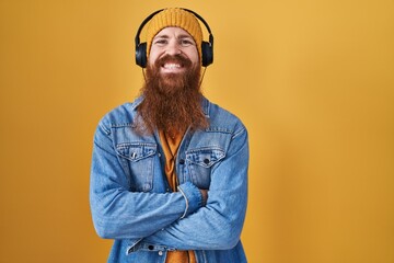 Caucasian man with long beard listening to music using headphones happy face smiling with crossed arms looking at the camera. positive person.