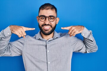 Naklejka premium Middle east man with beard standing over blue background smiling cheerful showing and pointing with fingers teeth and mouth. dental health concept.