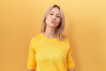 Obraz premium Young caucasian woman wearing yellow sweater looking at the camera blowing a kiss on air being lovely and sexy. love expression.