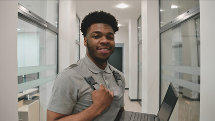 African CCTV cameras installer in uniform stands in corridor, smiles and looks at camera. He sets...