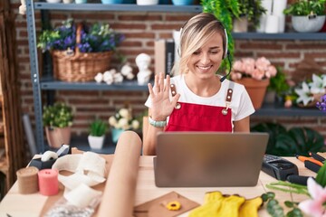 Young blonde woman working at florist shop doing video call looking positive and happy standing and smiling with a confident smile showing teeth