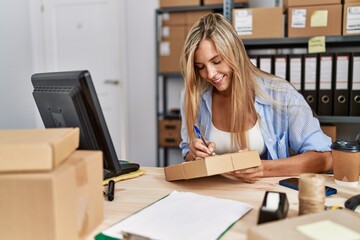 Young blonde woman ecommerce business worker writing on package at office