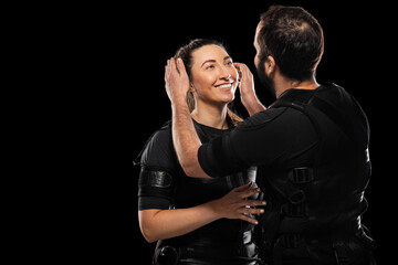 Couple in love wearing electric muscular stimulation suits. EMS fitness man and woman posing against black background.