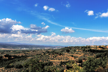 wide angle view of a wide Umbrian landscape with cultivated hills and roofs of a small town under a blue sky and some clouds