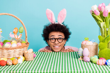 Photo of young man student hide desk basket drawing eggs spring easter funny ears rabbit near fresh...