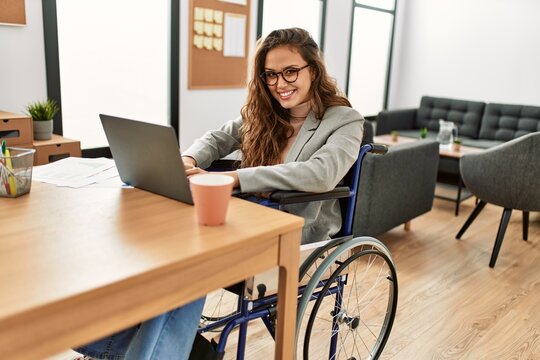 Young beautiful hispanic woman business worker using laptop sitting on wheelchair at office