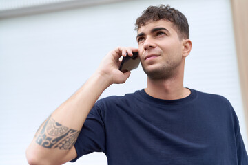 Young hispanic man talking on smartphone with serious expression at street