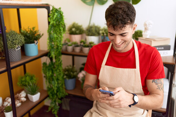 Fototapeta premium Young hispanic man florist smiling confident using smartphone at flower shop