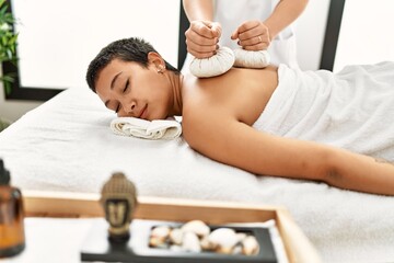 Obraz na płótnie Canvas Young hispanic woman having back massage using thai bags at beauty center