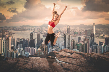 Fototapeta na wymiar A blond girl jumping up on rocks in front of a cityscape