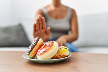 Young hispanic woman rejecting doughnut at home