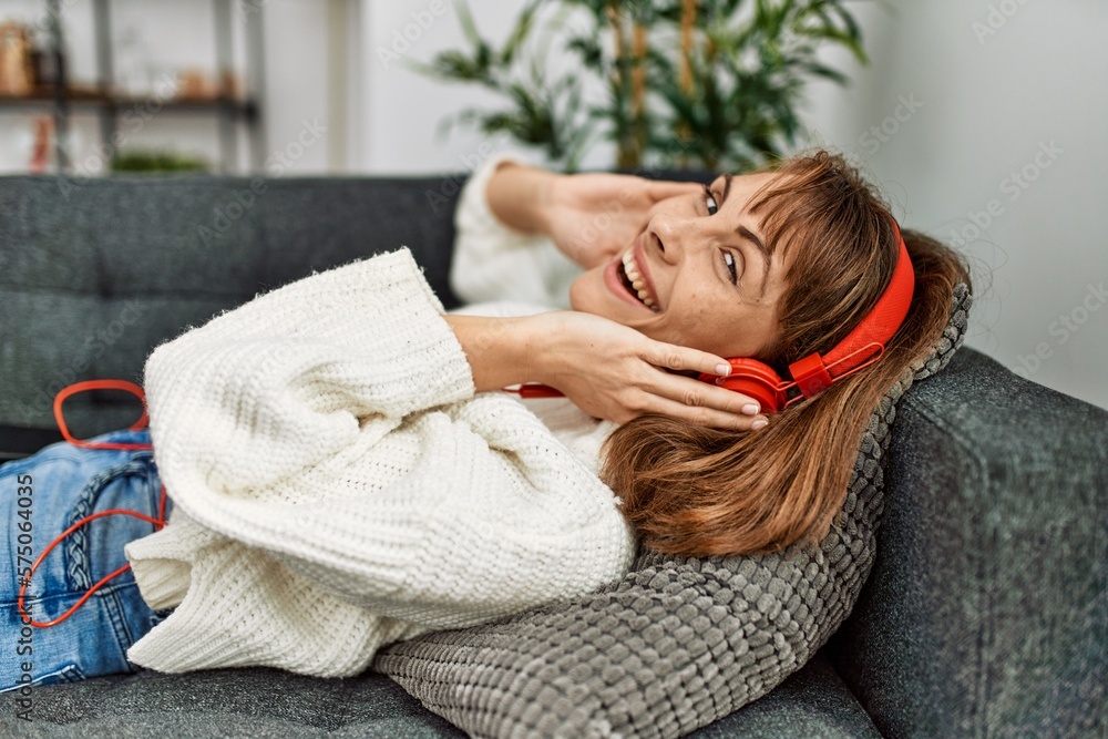 Sticker Young caucasian woman listening to music lying on sofa at home