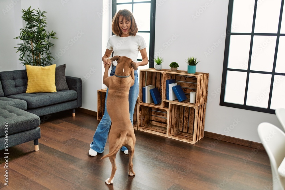 Wall mural young caucasian woman smiling confident dancing with dog at home