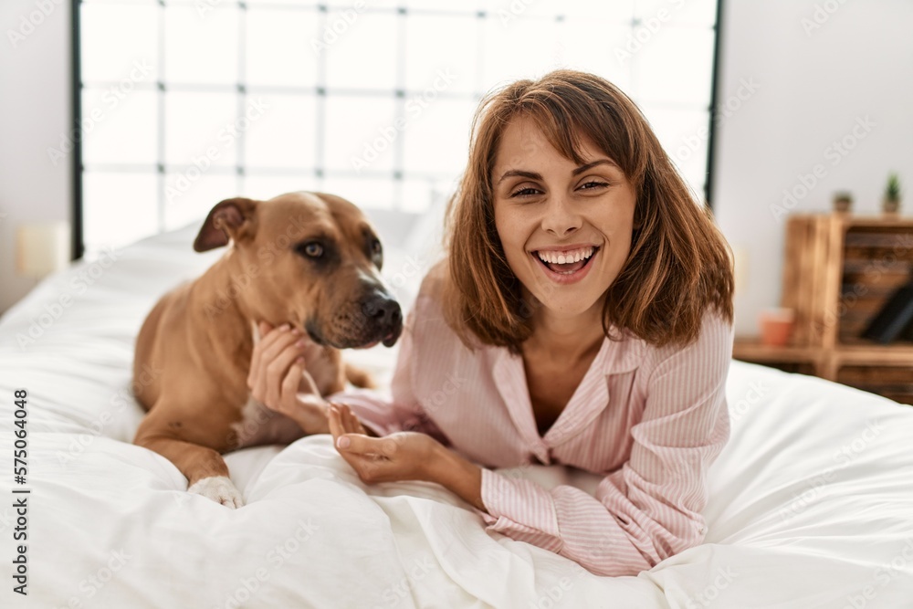 Poster Young caucasian woman smiling confident lying on bed with dog at bedroom