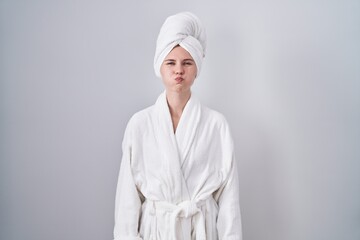 Blonde caucasian woman wearing bathrobe puffing cheeks with funny face. mouth inflated with air, crazy expression. - obrazy, fototapety, plakaty