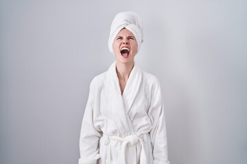 Blonde caucasian woman wearing bathrobe angry and mad screaming frustrated and furious, shouting with anger. rage and aggressive concept.