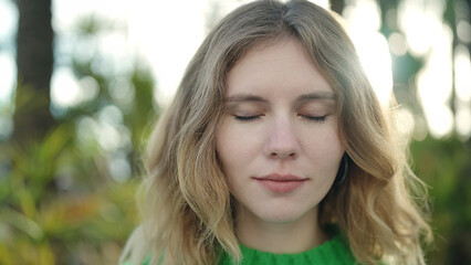 Young blonde woman breathing with closed eyes at park