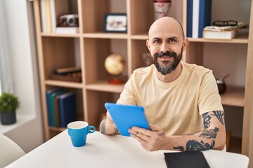 Young bald man using touchpad sitting on table at home