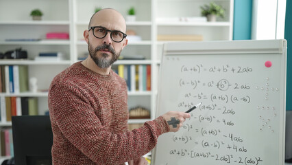 Young bald man teacher teaching maths on magnetic board at university classroom