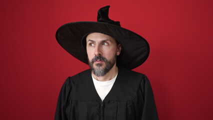 Young bald man wearing wizard costume standing with fear expression over isolated red background