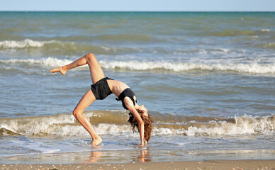barefoot girl in black swimsuit from rhythmic gymnastics exercises on the seashore