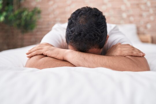 Young hispanic man stressed lying on bed at bedroom