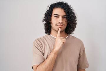 Fototapeta na wymiar Hispanic man with curly hair standing over white background thinking concentrated about doubt with finger on chin and looking up wondering
