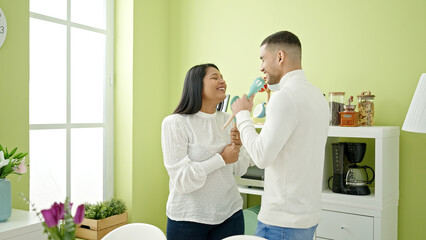 Man and woman couple singing song using cook utensil as a microphone at home