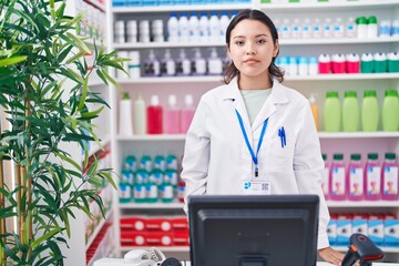 Hispanic young woman working at pharmacy drugstore with serious expression on face. simple and natural looking at the camera.