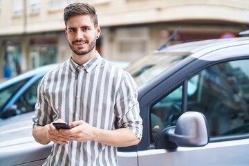 Fototapeta na wymiar Young caucasian man using smartphone leaning on car at street