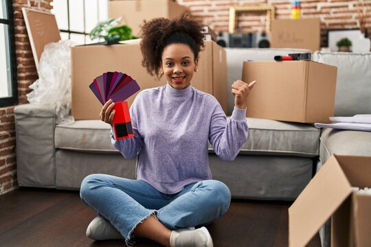 Young african american woman moving to a new home choosing colors pointing thumb up to the side smiling happy with open mouth