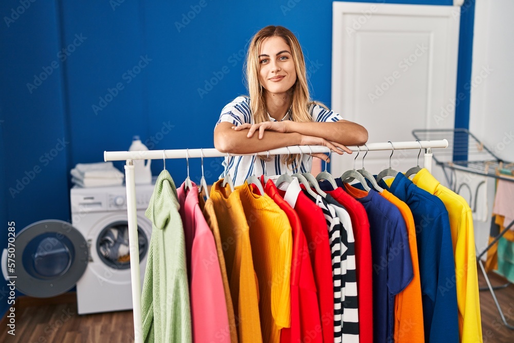 Sticker young blonde woman at laundry room with clean clothes relaxed with serious expression on face. simpl