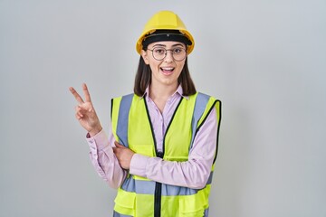 Hispanic girl wearing builder uniform and hardhat smiling with happy face winking at the camera...