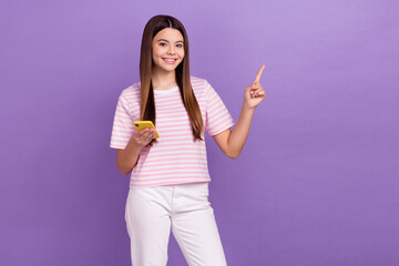 Photo of funny sweet girl dressed striped t-shirt writing modern device pointing empty space isolated purple color background