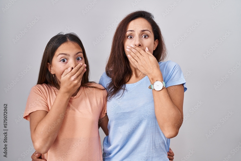 Sticker young mother and daughter standing over white background shocked covering mouth with hands for mista